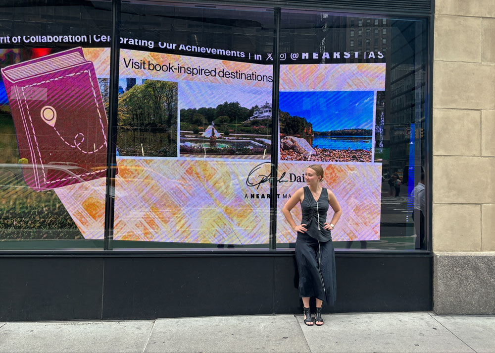 Zora Lee stands in front of a NYC window display showcasing one of the articles she wrote for Oprah Daily, about book-cations