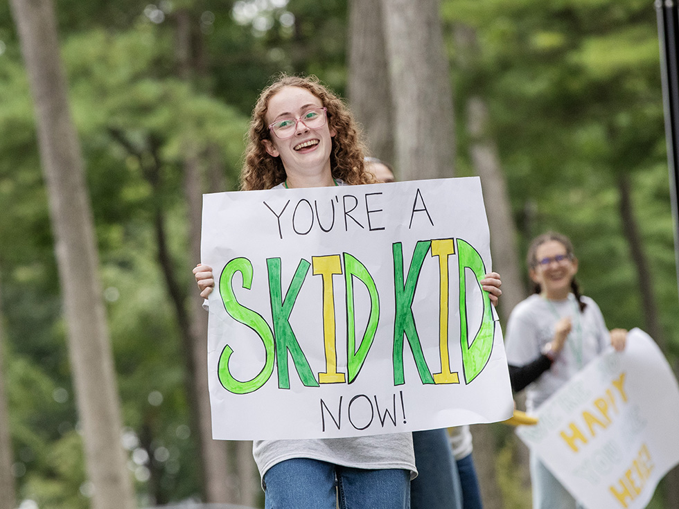 A student holding a sign "You're a Skid kid now!"