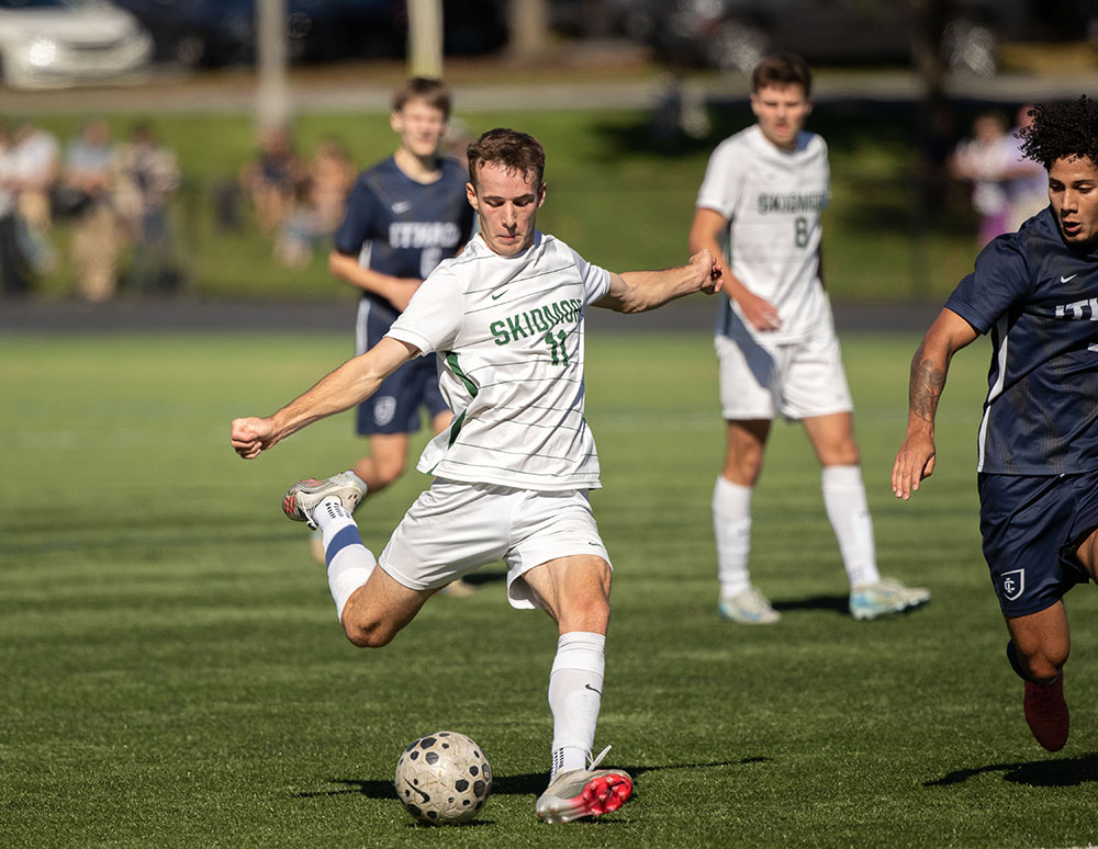 Men's soccer players during a game on a grass soccer field, one player making a play to kick the ball. 