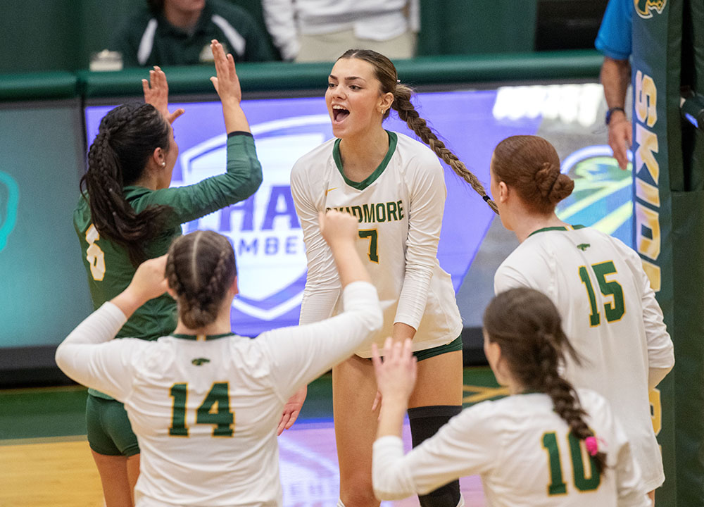 Five women's volleyball players come together on the court to celebrate a point scored.