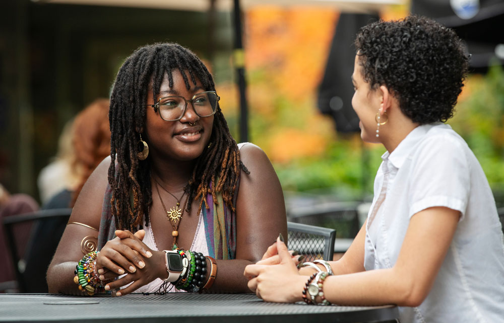 Sela Safo smiles as she sits outside at a table talking with a friend
