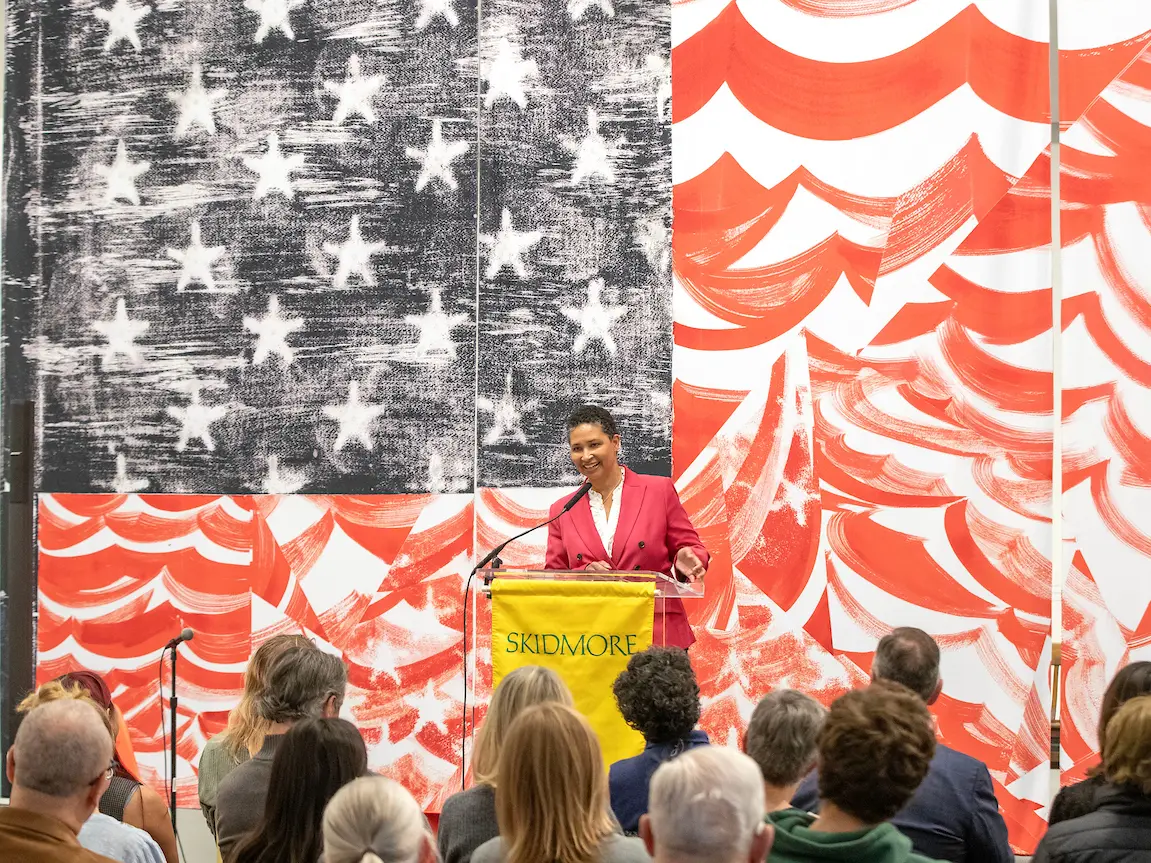 Danielle Allen speaking at a podium in front of an American flag-inspired design in front of an audience.
