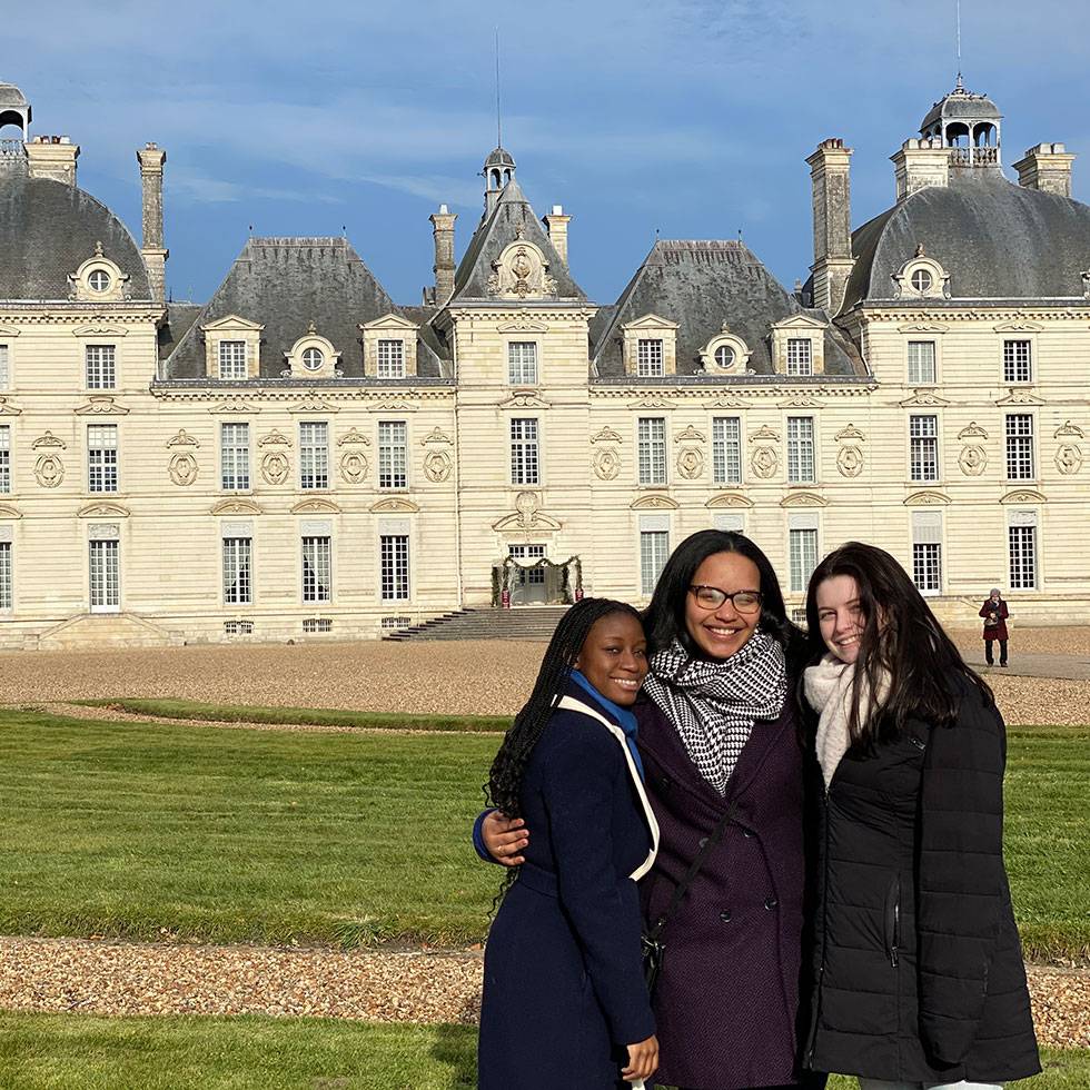 Three students pose together in front of a historic château in France on a sunny day.