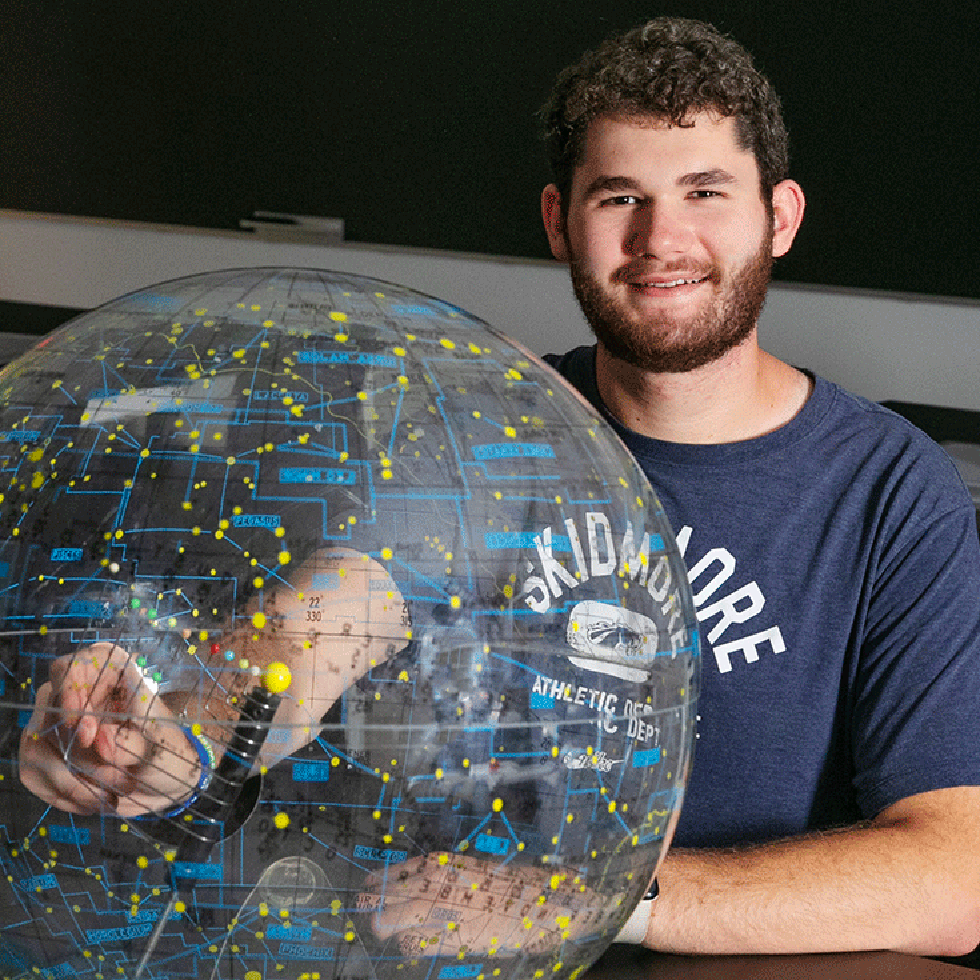 Skidmore College physics student smiles while working with a transparent celestial globe marked with constellations and stars.