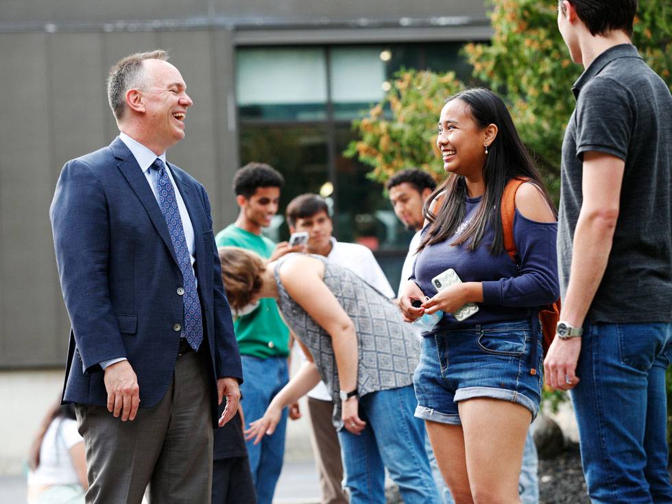 President Conner stands outside, laughing while talking to students.