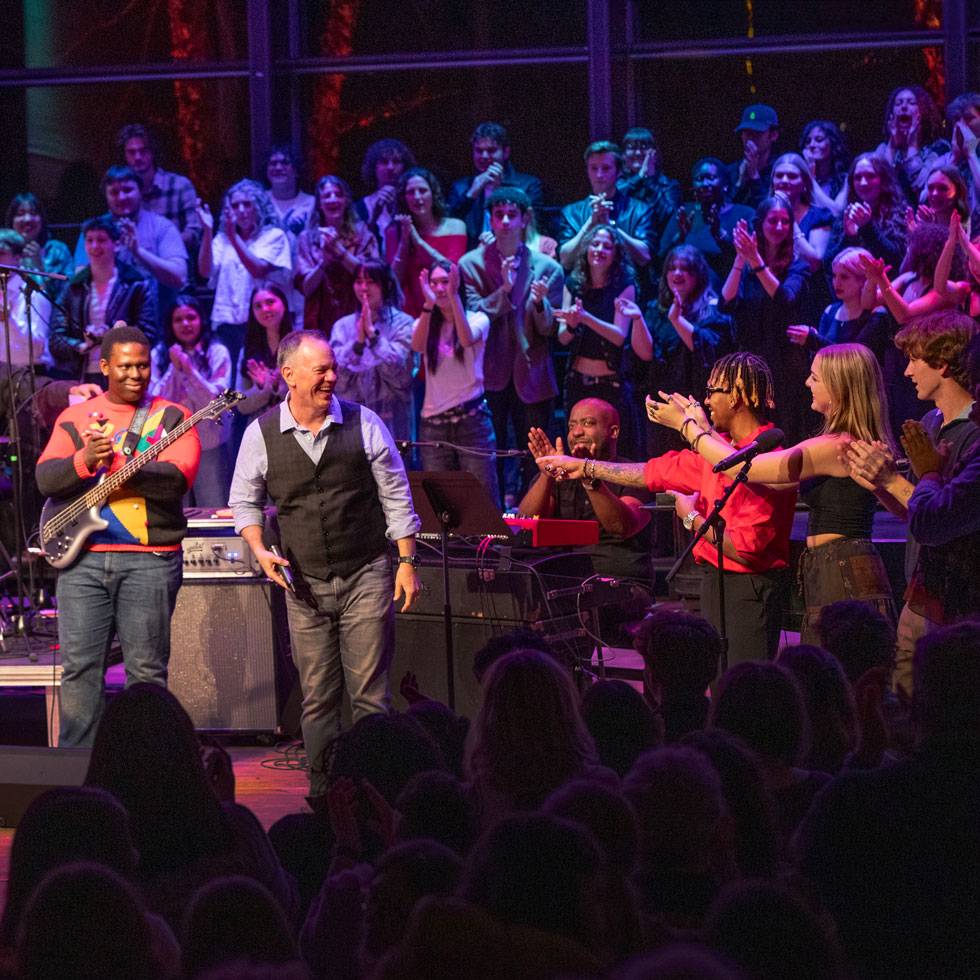 President Conner on stage performing with a large group of student and faculty musicians during an evening performance.