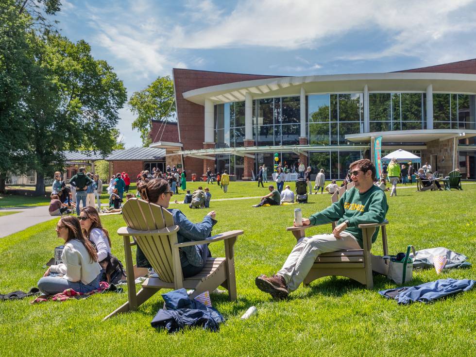 A group of skidmore alumni sit in adirondack chairs socializing on a beautiful sunny day
