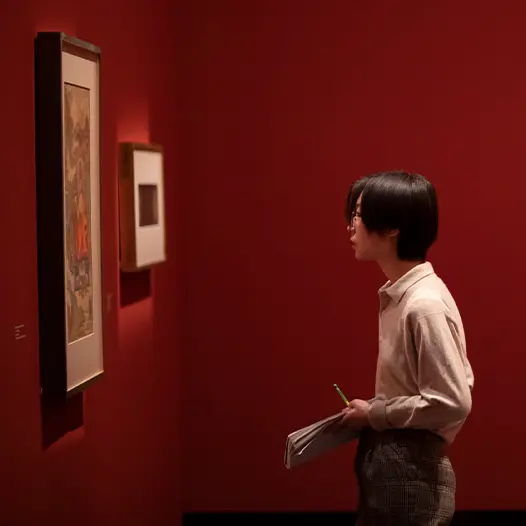 A Skidmore student takes notes while observing an art installation in a gallery space painted dark red.