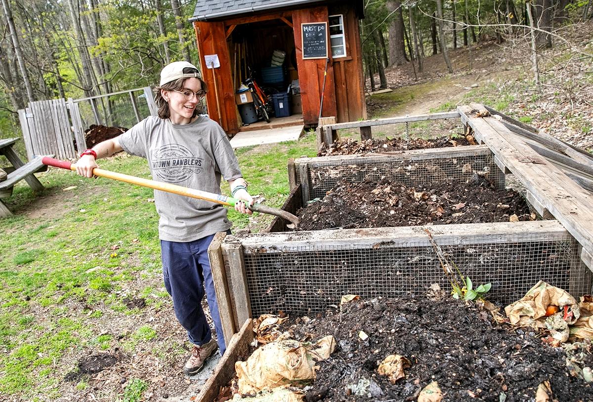 Student turning compost with a pitchfork at Skidmore’s composting station as part of the college’s sustainability efforts.