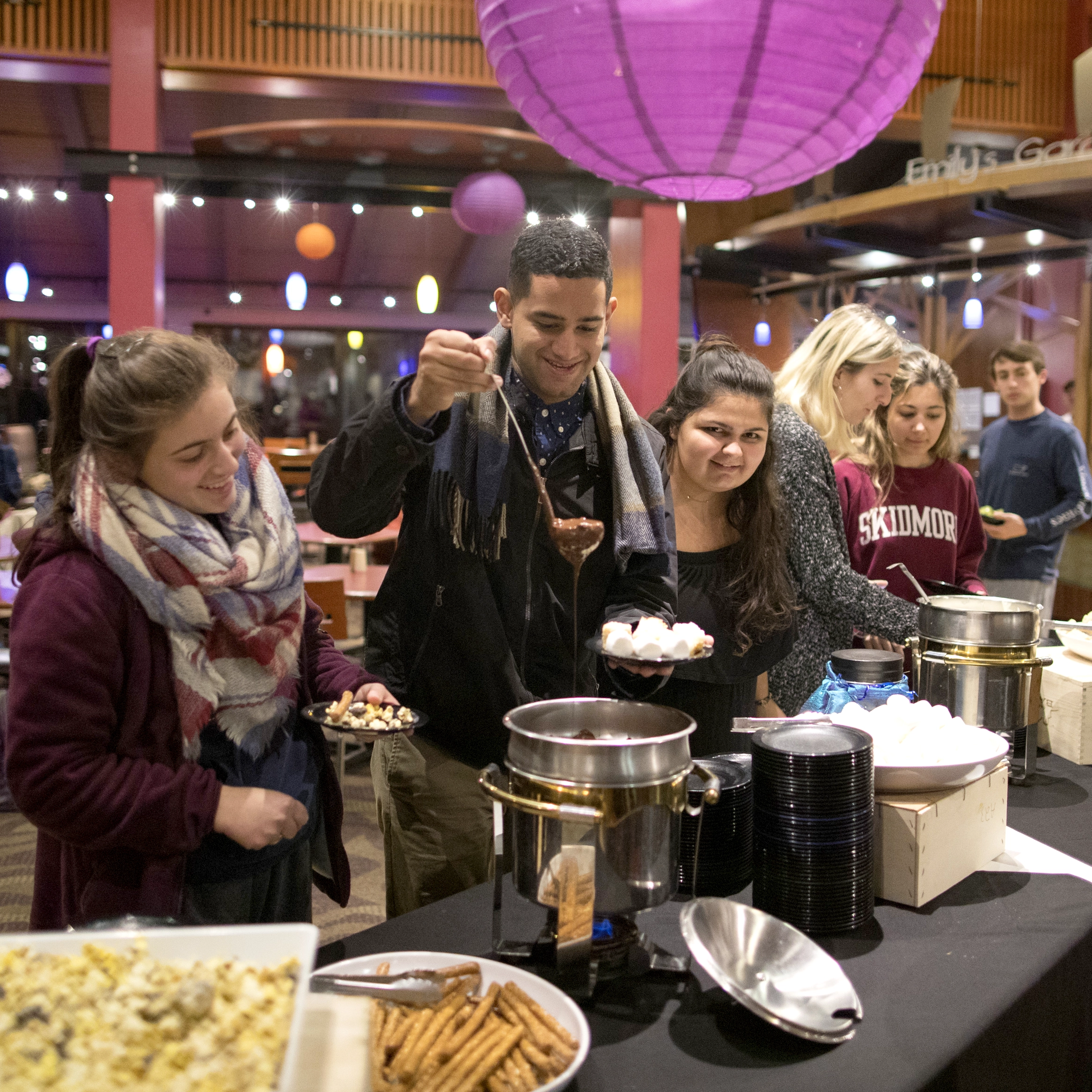 Skidmore students enjoying a themed dining event, scooping chocolate from a fountain at a dessert station.