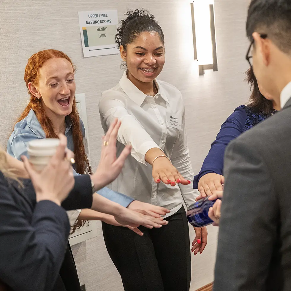Students participate in a pre-event huddle, smiling and placing their hands together during a career networking event.