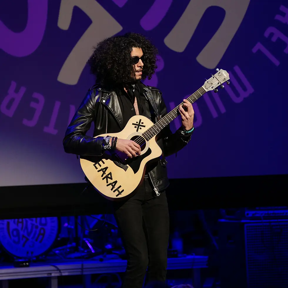 A student in sunglasses and a leather jacket plays guitar onstage during Skidmania, an annual concert at Skidmore College.