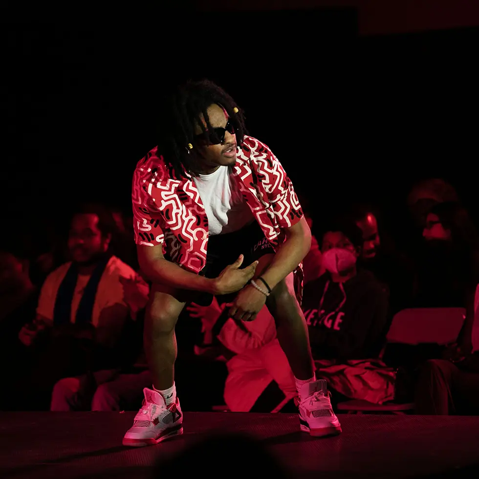 A student in bold red and white patterned clothing strikes a pose under dramatic red lighting during Skidmore’s Ujima fashion show.