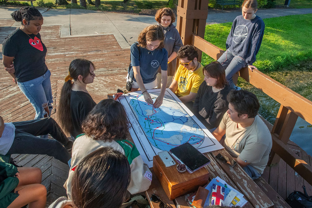 Students gather around a map during a college cartography class held outside during the summer under a pavillion