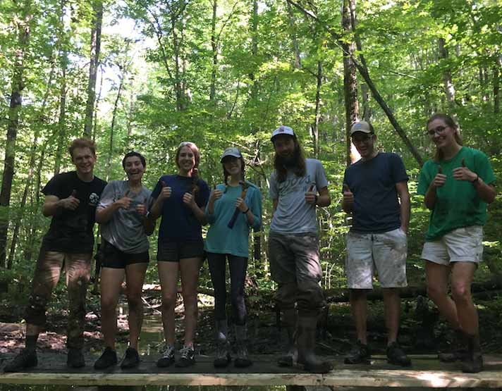7 sustainability people- staff and students- stand lined up on a boardwalk they just repaired with thumbs up