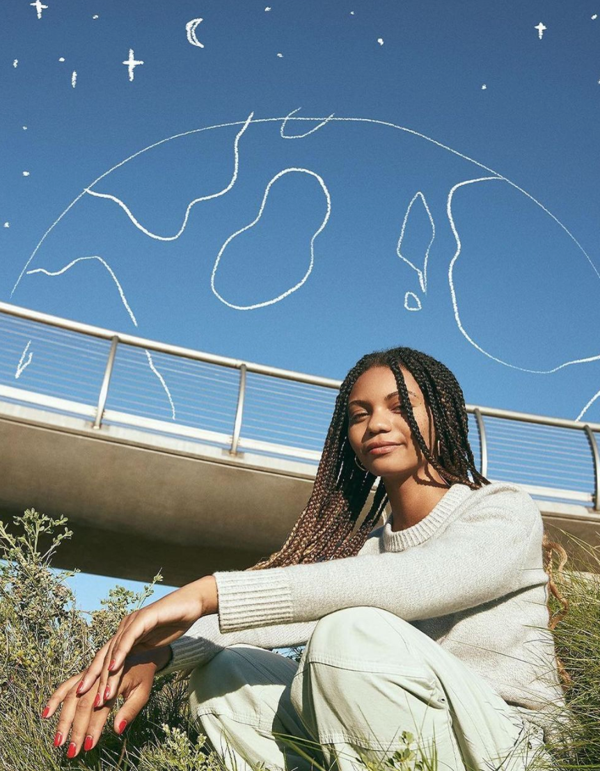 Photo of Leah Thomas in a field with blue sky and outline of the earth in white