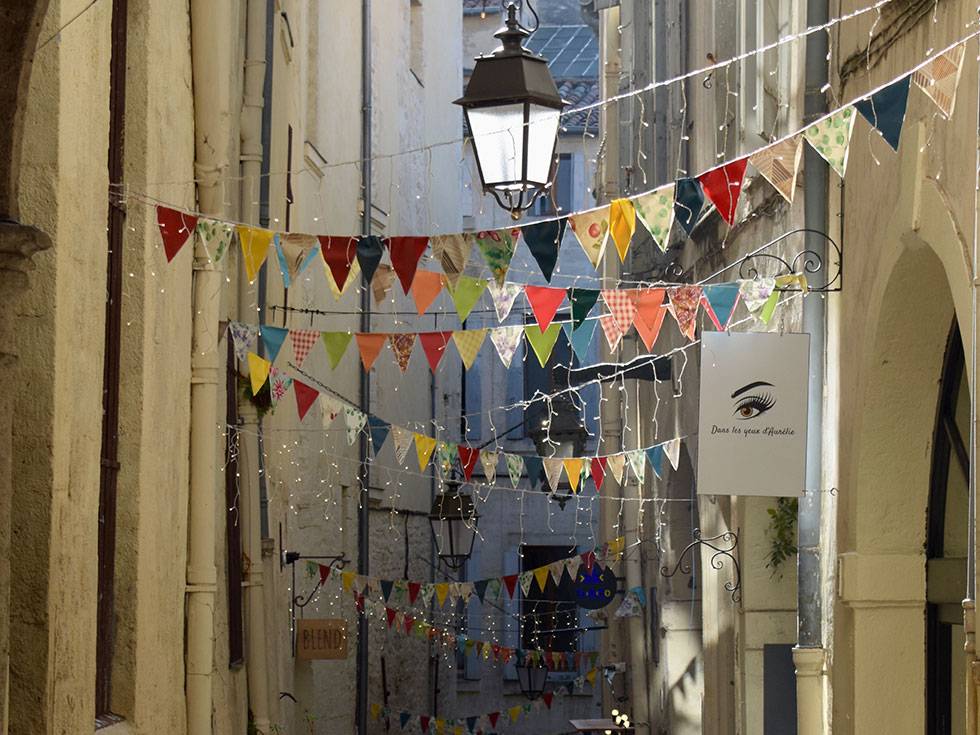 Colorful banners line a historic alley in a French town