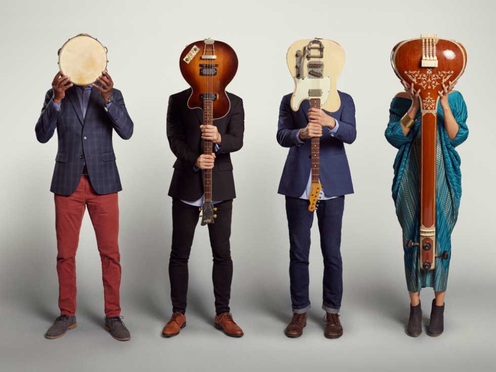 Members of American Patchwork Quartet stand against a plain backdrop, holding instruments in front of their faces.