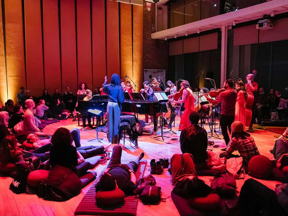 Musicians perform during a Somi healing concert, with audience members seated on the floor around the stage.