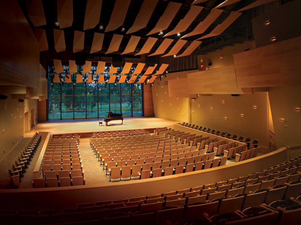 Empty Zankel Music Center concert hall with rows of seats, a grand piano onstage, and tall windows behind the stage.